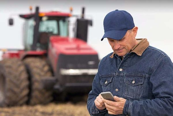 Farmer looking at his phone with a tractor in the background