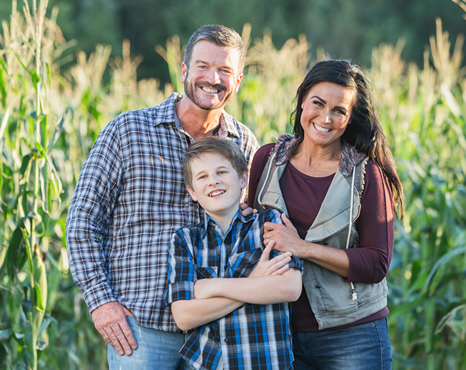 Farmer and family standing in front of corn field smiling